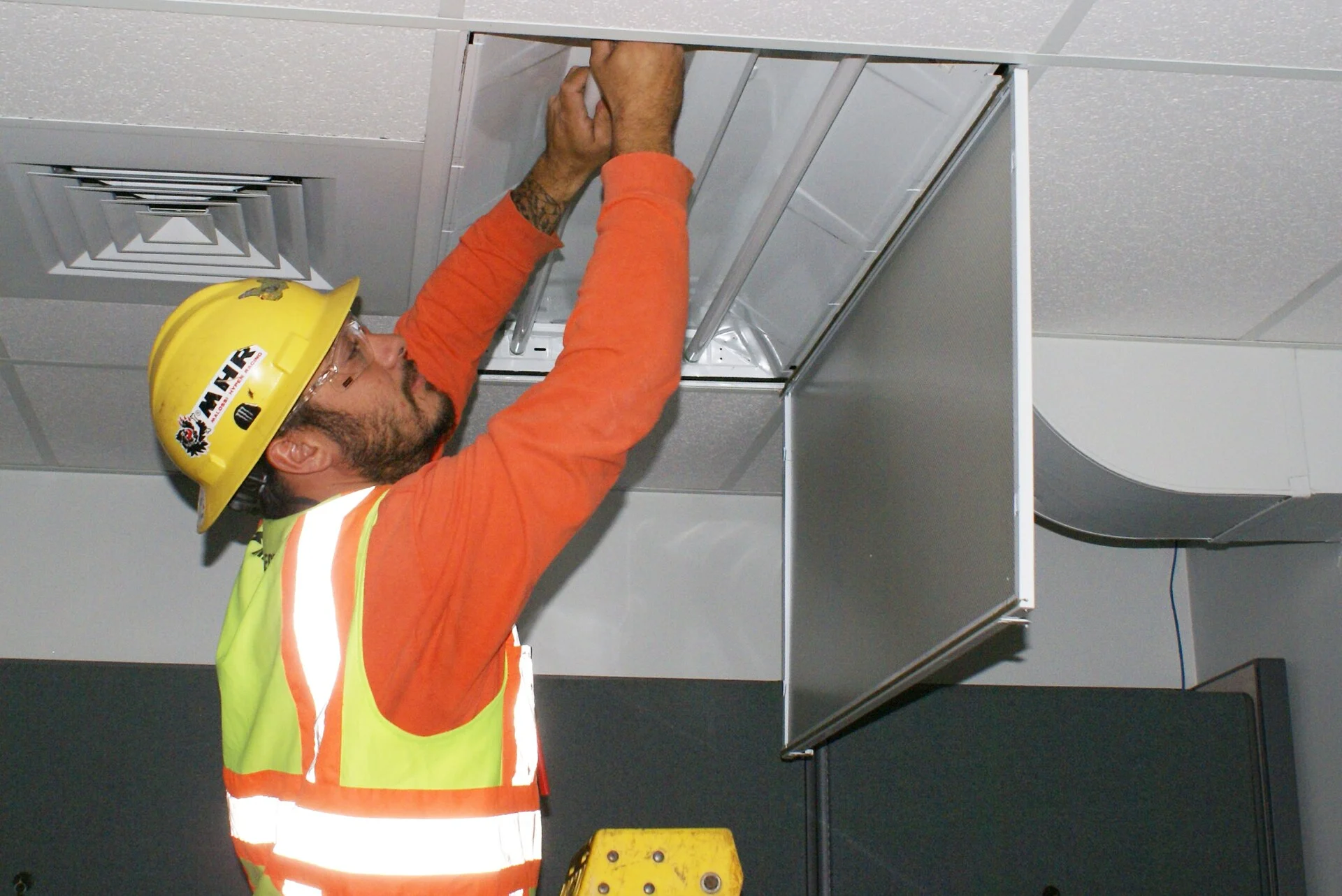An electrician replacing a ceiling light ballast during a lighting retrofit
