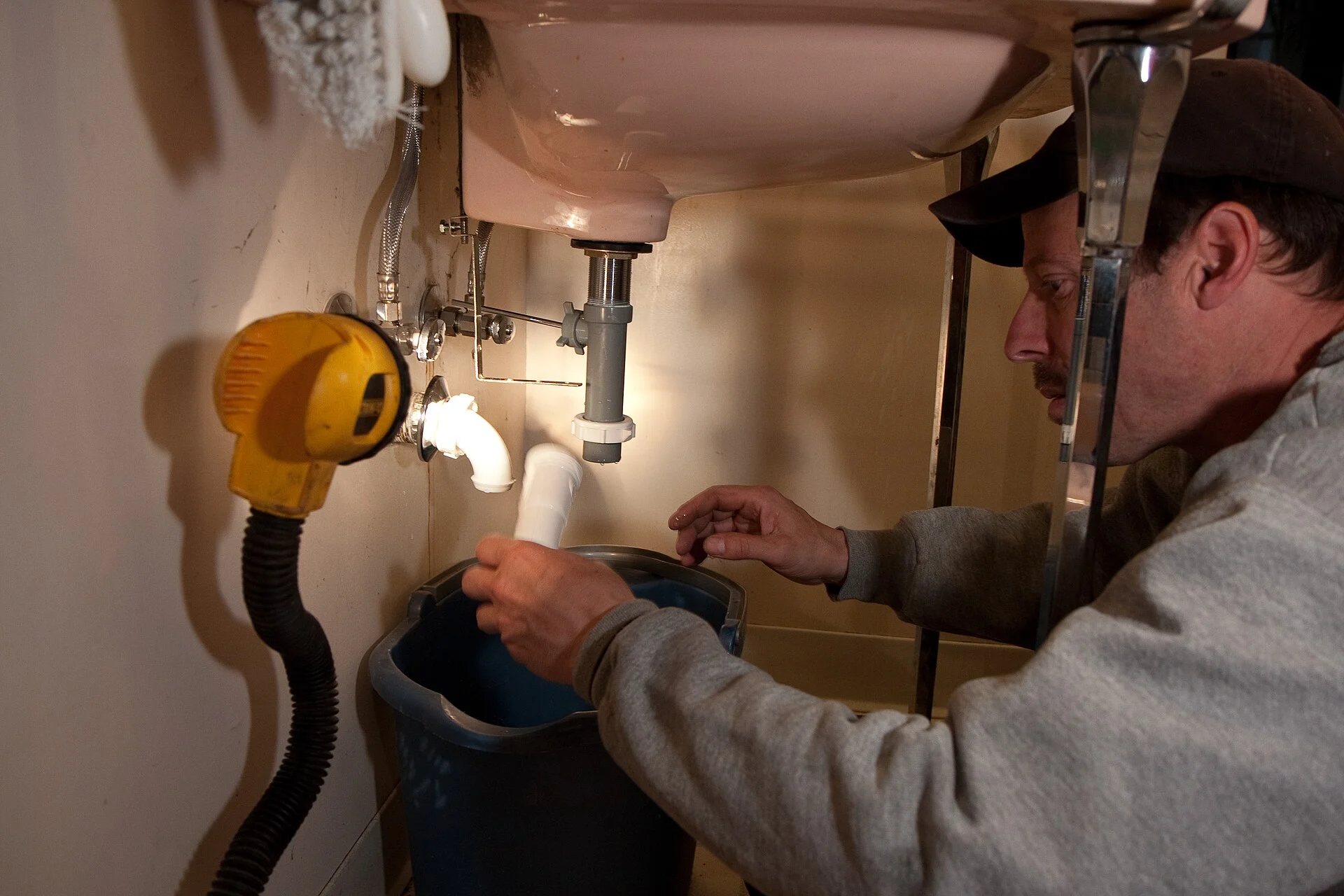 A plumber fitting a white drain trap beneath a bathroom sink